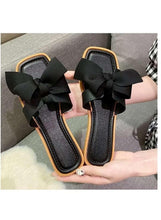 Black wedge sandals with large bow and open toe, tan-trimmed sides, pair shown