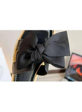 Black wedge sandals with large bow detail over open toe and tan edge sole