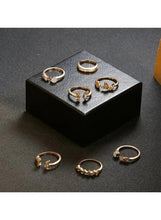 Gold-tone fashion ring set with clear stones on black display box, six rings visible.