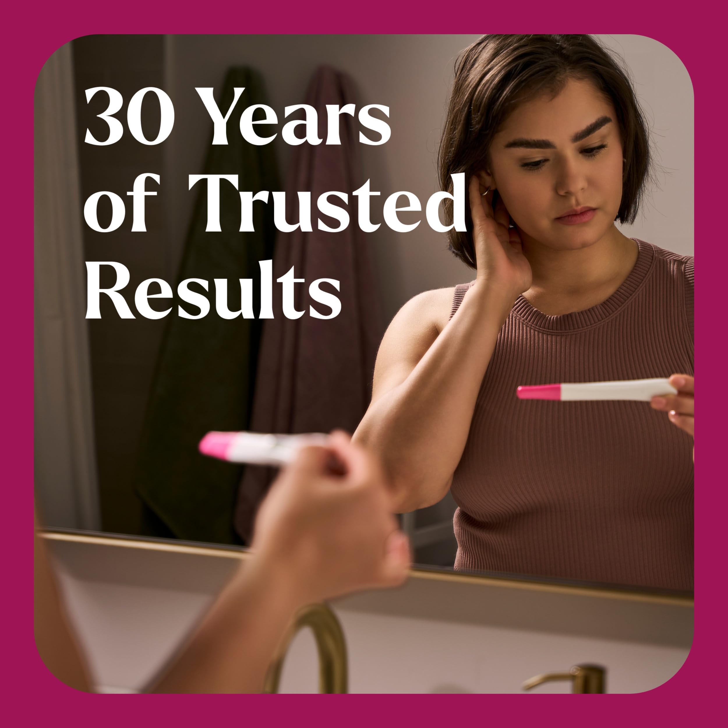 Woman looking in bathroom mirror holding a First Response pregnancy test UAE with thoughtful concerned expression