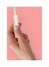 Hand holding a white gas relief tube applicator against a pink background