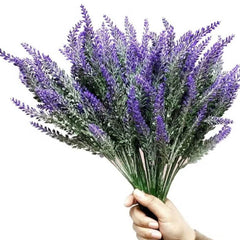 Hand holding a bouquet of artificial lavender flowers decor with green stems and purple blossoms