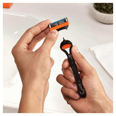 Hands attaching an orange Gillette razor cartridge to black handle over sink Gillette Fusion razor blades 8 pack