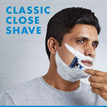 Man using a blue cartridge razor while shaving, foam on his cheek