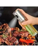 Glass olive oil sprayer bottle with stainless cap spraying over grilled food