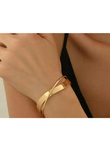 Gold alloy cuff bracelet worn on wrist, wide polished band.
