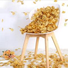 Gold artificial rose petals spilling from a white chair on a soft white carpet with a small bouquet of flowers nearby
