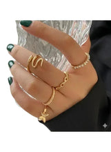 Gold-tone fashion ring set with letter-style and charm rings, shown on hand