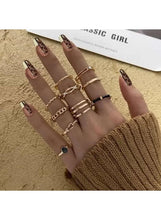 Gold-tone fashion ring set laid on hand, slim bands with black and blue stones.
