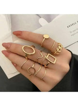 Gold-tone minimalist geometric rings on hand, including round, oval, and square bezel styles.