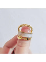 Gold-tone stacked rings with a pink cabochon accent and textured chain band