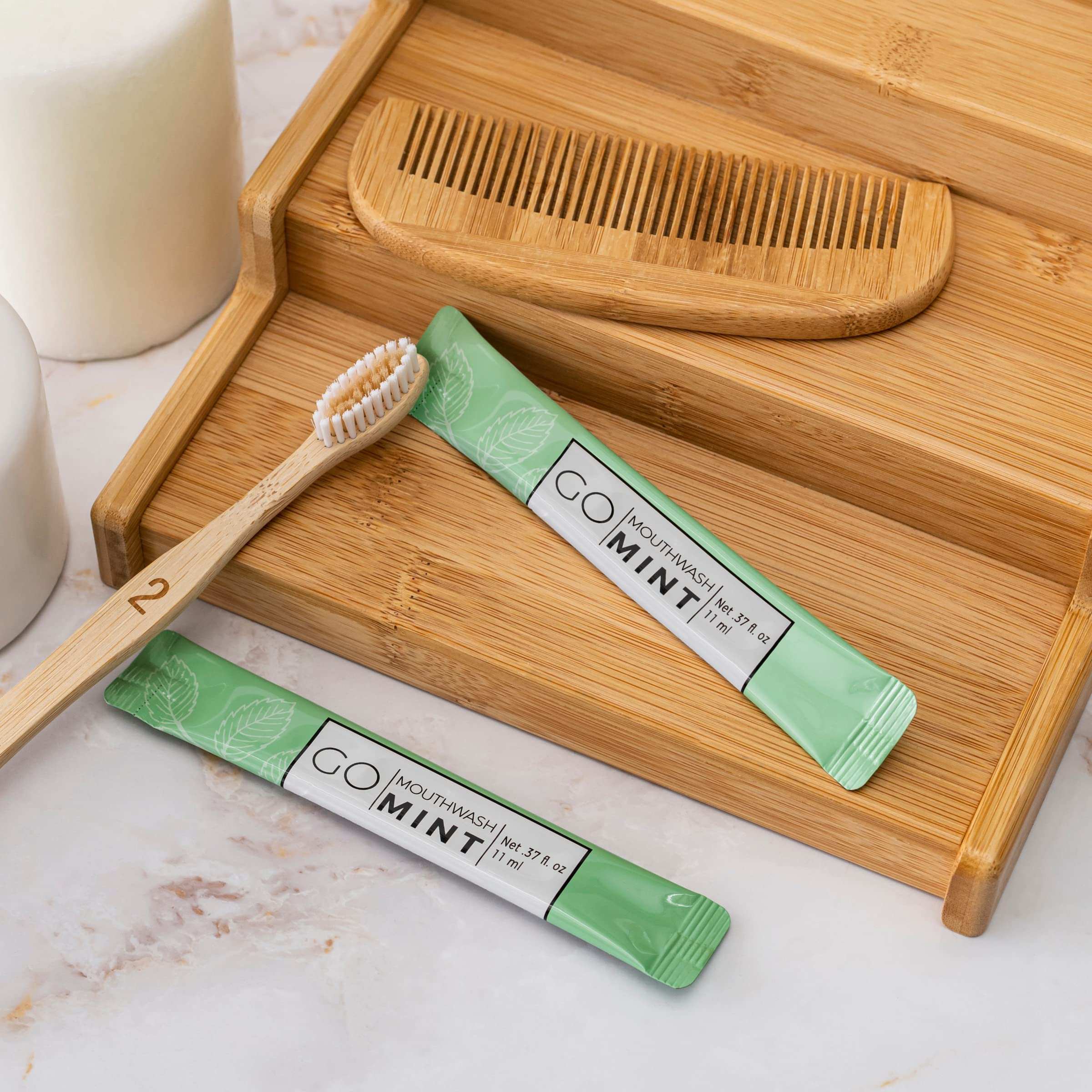 Go Essentials travel mouthwash packets mint sachets with bamboo toothbrush and wooden comb on wooden tray