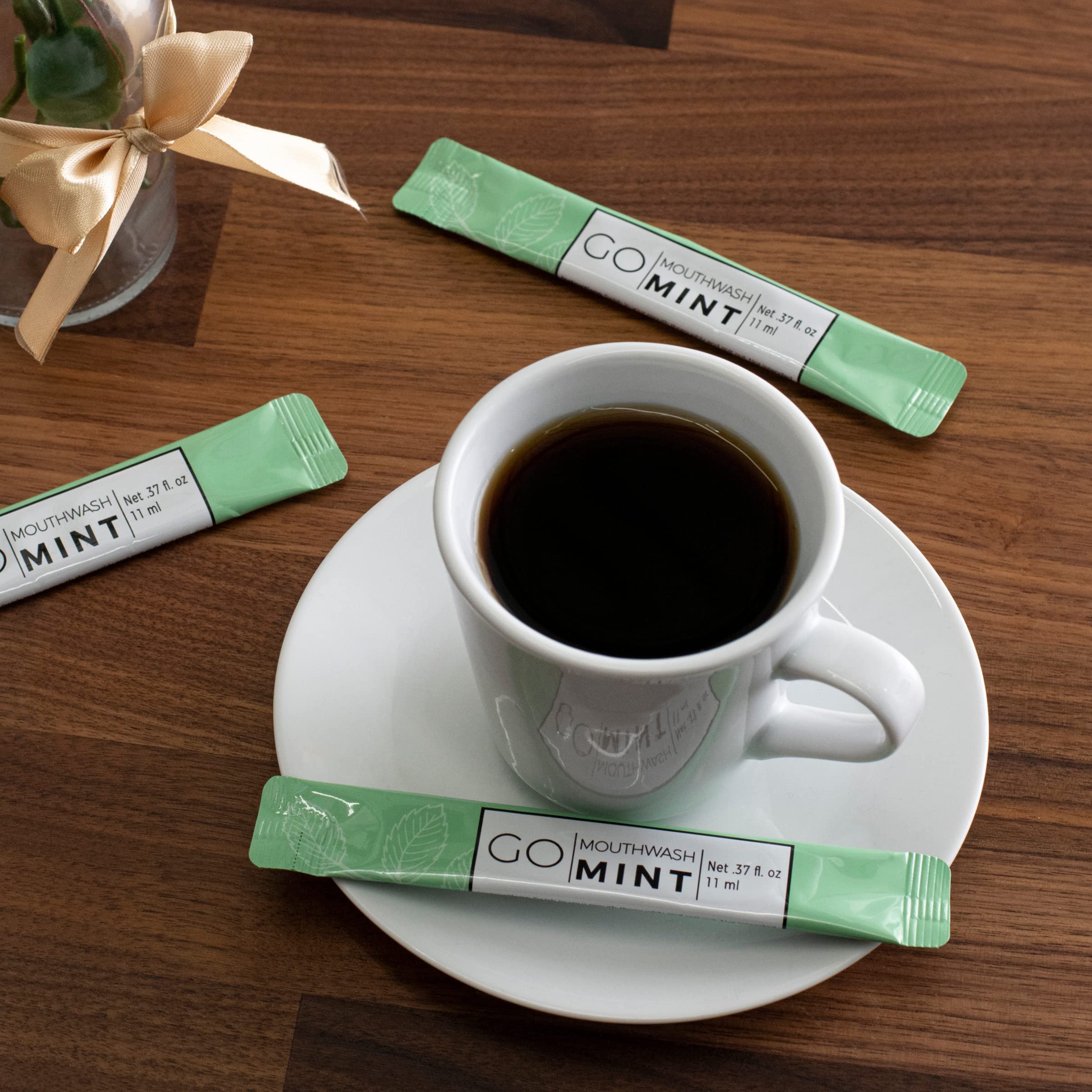 Go Essentials mint single use travel mouthwash packets beside a coffee cup on a wooden table