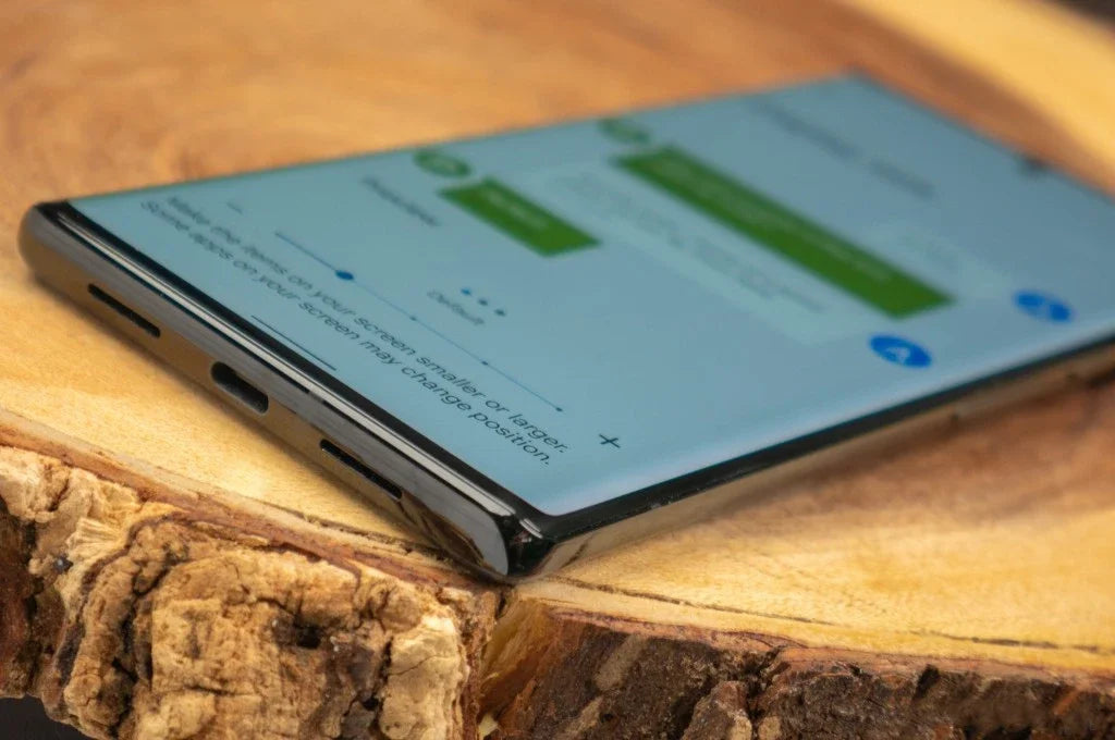 Close up of Google Pixel 6 Pro 5G unlocked laying on a wooden slab showing curved edge USB C port and messaging screen