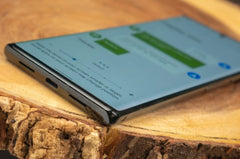 Close up of Google Pixel 6 Pro 5G unlocked laying on a wooden slab showing curved edge USB C port and messaging screen