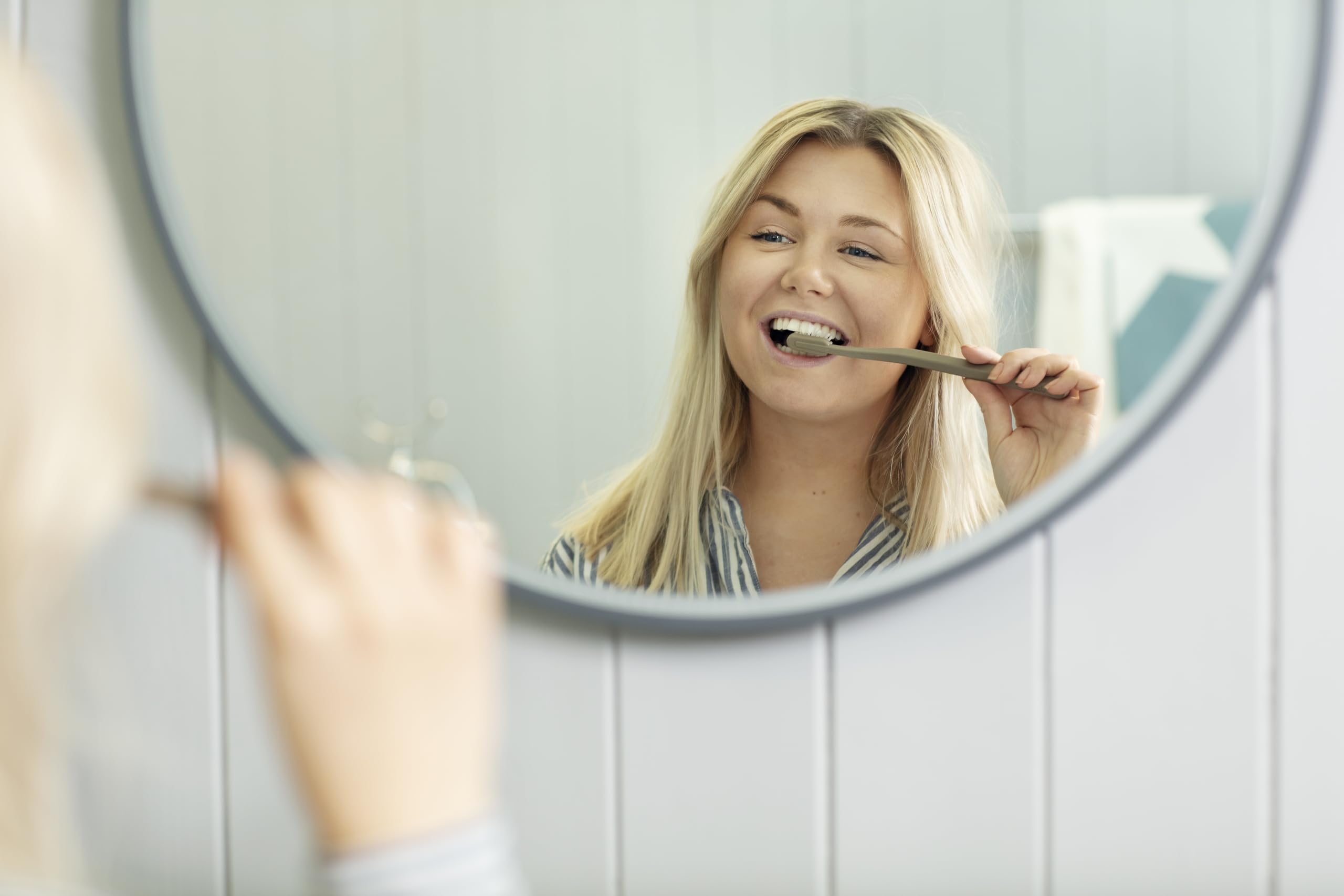 Woman smiling while brushing teeth in mirror with eco friendly toothbrush UAE by Jordan