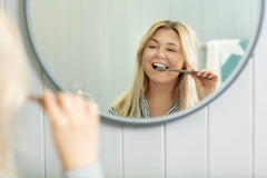 Woman smiling while brushing teeth in mirror with eco friendly toothbrush UAE by Jordan