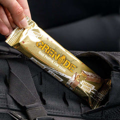 Hand placing a Grenade Carb Killa protein bar Caramel Chaos flavor in gold wrapper into a black backpack