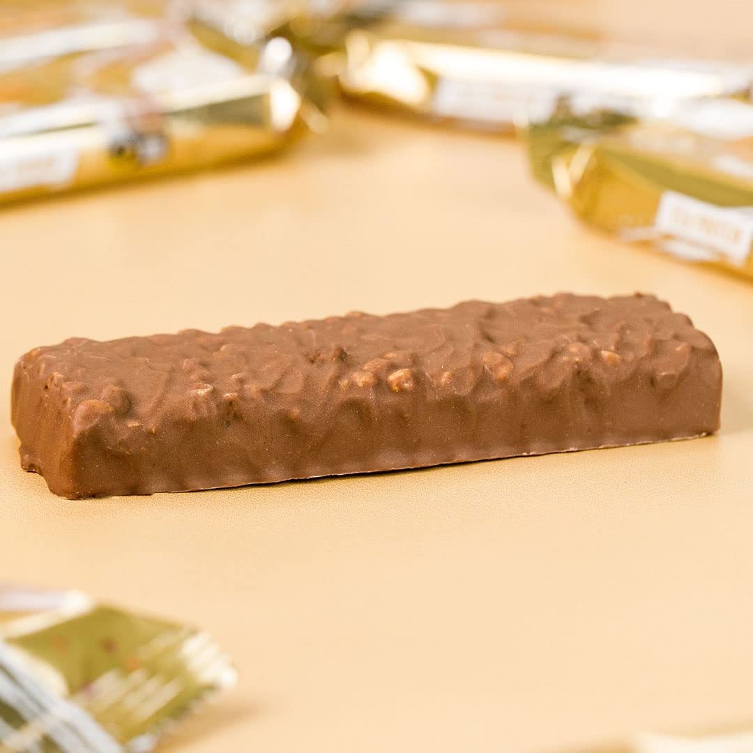Grenade Carb Killa protein bar unwrapped chocolate coated with nut pieces on beige surface with gold wrappers