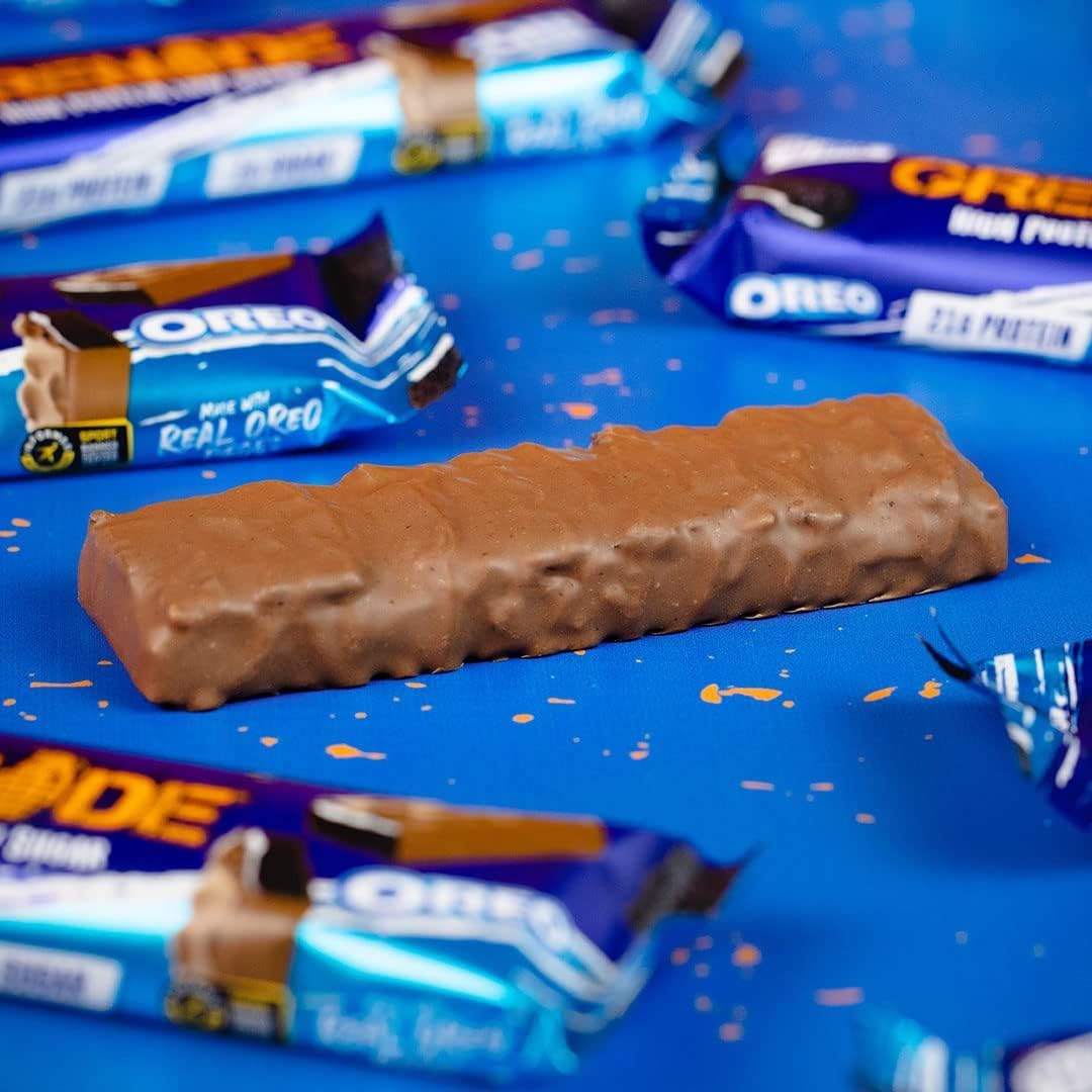 Chocolate coated grenade oreo protein bar on blue backdrop with Oreo wrappers and opened package