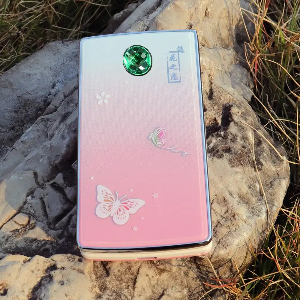 Mumzar pink butterfly clamshell phone on rock showing decorative back panel and green camera gem women flip phone dual sim