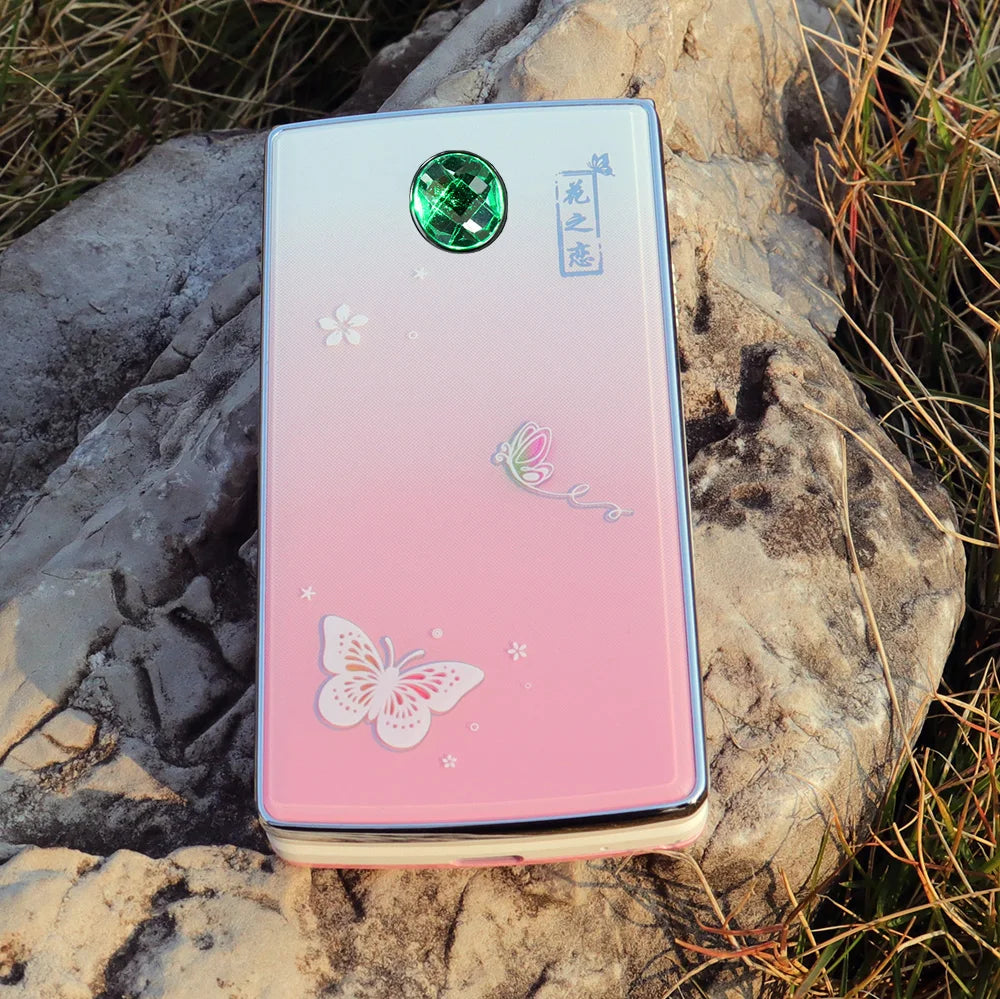 Mumzar pink butterfly clamshell phone on rock showing decorative back panel and green camera gem women flip phone dual sim