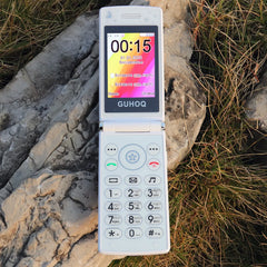 White Mumzar clamshell mobile on rocks and grass showing keypad and screen women flip phone dual sim