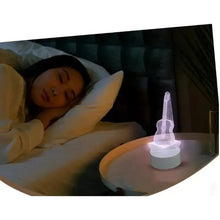 LED guitar night light glowing purple on round base beside a pillow and bed