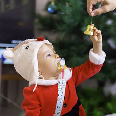 Baby in reindeer hat and red holiday outfit reaching for a bell with baby pacifier clips set attached to pacifier