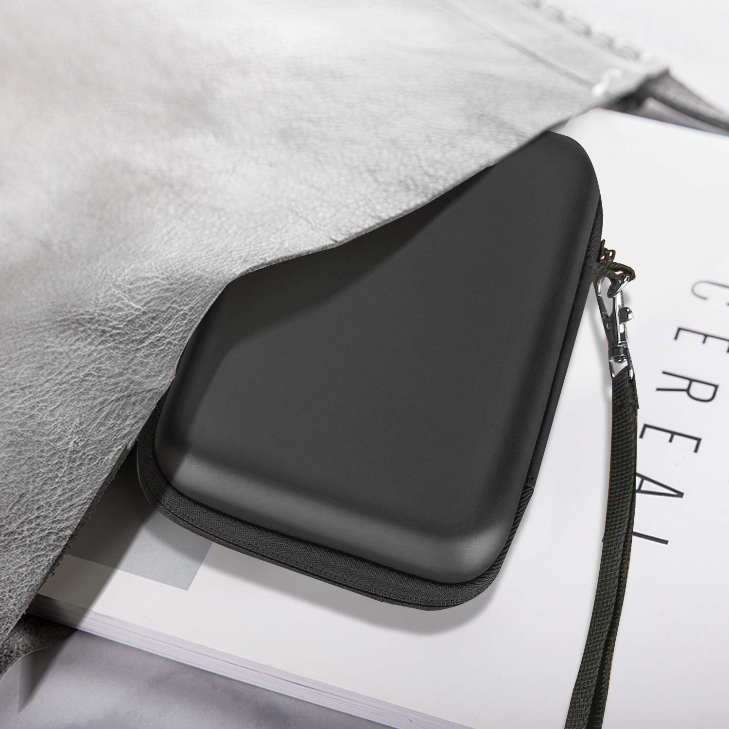 Black hard disk carrying case for travel with zipper and wrist strap partially tucked under a gray bag