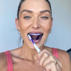 Woman applying Hismile v34 Colour Corrector purple gel with toothbrush to teeth for whitening treatment