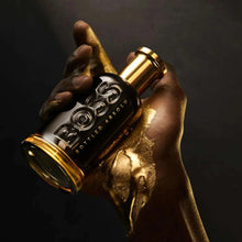 Perfume bottle with dark glass and gold cap held in hands, embossed logo