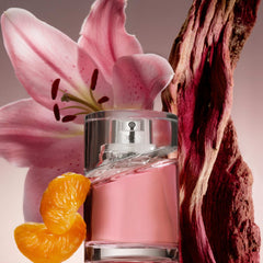 Hugo Boss Femme perfume bottle with pink liquid next to a pink flower, orange slices, and textured wood