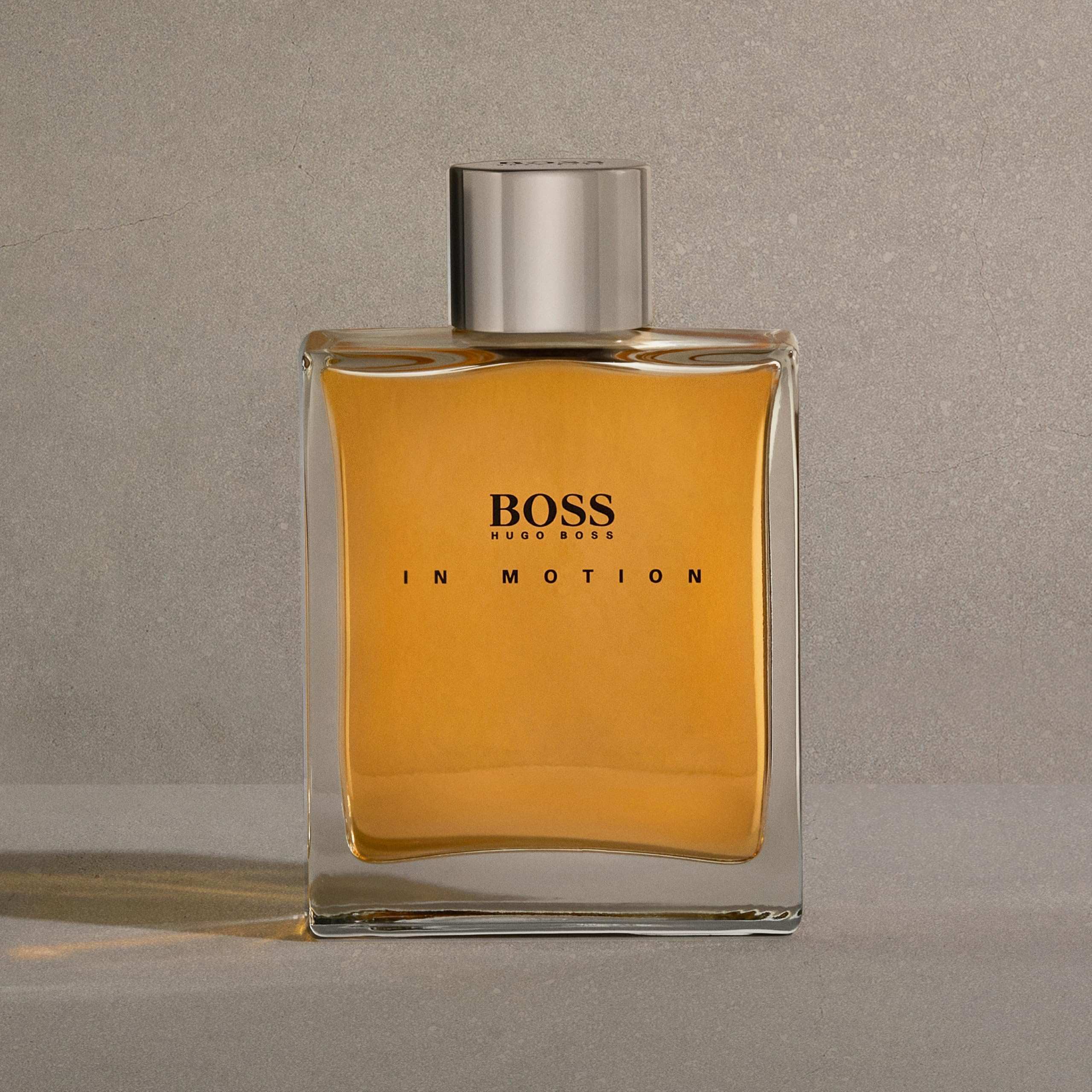 Hugo Boss In Motion for men fragrance bottle with amber liquid and silver cap on gray background
