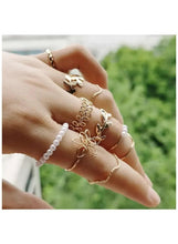 Gold-tone floral and leaf rings on hand, layered with one pearl-style ring
