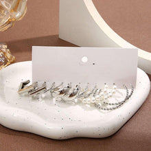 Silver-tone hoop and chain earrings with pearl details arranged on a white tray