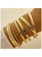 Gold tone bracelet set on wrist with multiple flat bangles and engraved details