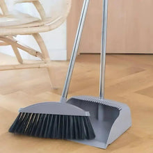 Wide dustpan with toothed edge and long-handled broom, dense dark bristles.