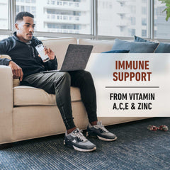 Man on couch drinking protein shake while using laptop with immune support label Isopure whey protein isolate