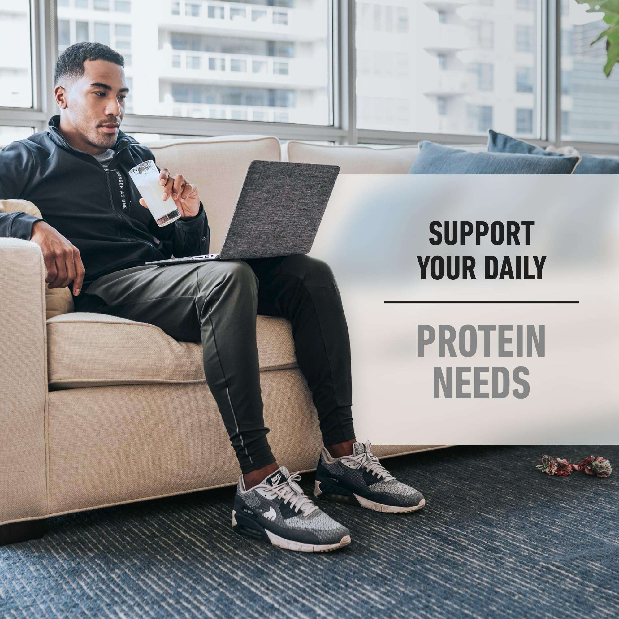 Isopure zero carb whey protein isolate shake in glass held by man on couch with laptop supporting daily protein needs