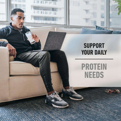 Isopure zero carb whey protein isolate shake in glass held by man on couch with laptop supporting daily protein needs