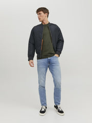 Man wearing green crew neck t-shirt men with black bomber jacket light blue jeans and black sneakers