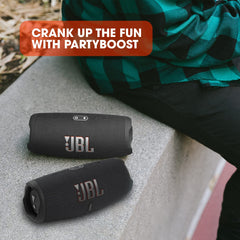 Two black JBL Charge 5 portable Bluetooth speakers placed on a concrete surface with a person wearing a green and black checkered shirt nearby