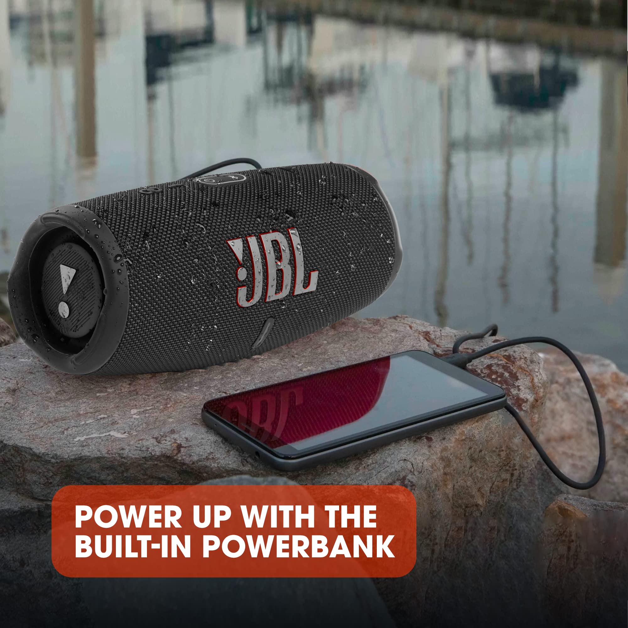 JBL Charge 5 portable Bluetooth speaker with built-in powerbank shown connected to a smartphone on a rock near water