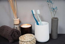 Toothbrushes in cups with white bristles and teal and blue handles, medium size.