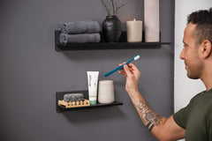 Jordan eco friendly toothbrush UAE held by a man in bathroom with toothpaste tube soap and folded towels on shelves