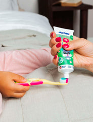 Jordan kids toothpaste for 0-5 years being squeezed onto a childs toothbrush by an adult