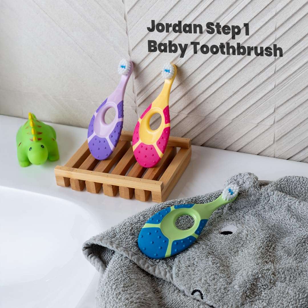 Jordan colorful Step 1 baby toothbrushes on bathroom tray and towel with toy dinosaur soft bristle toothbrush for infants