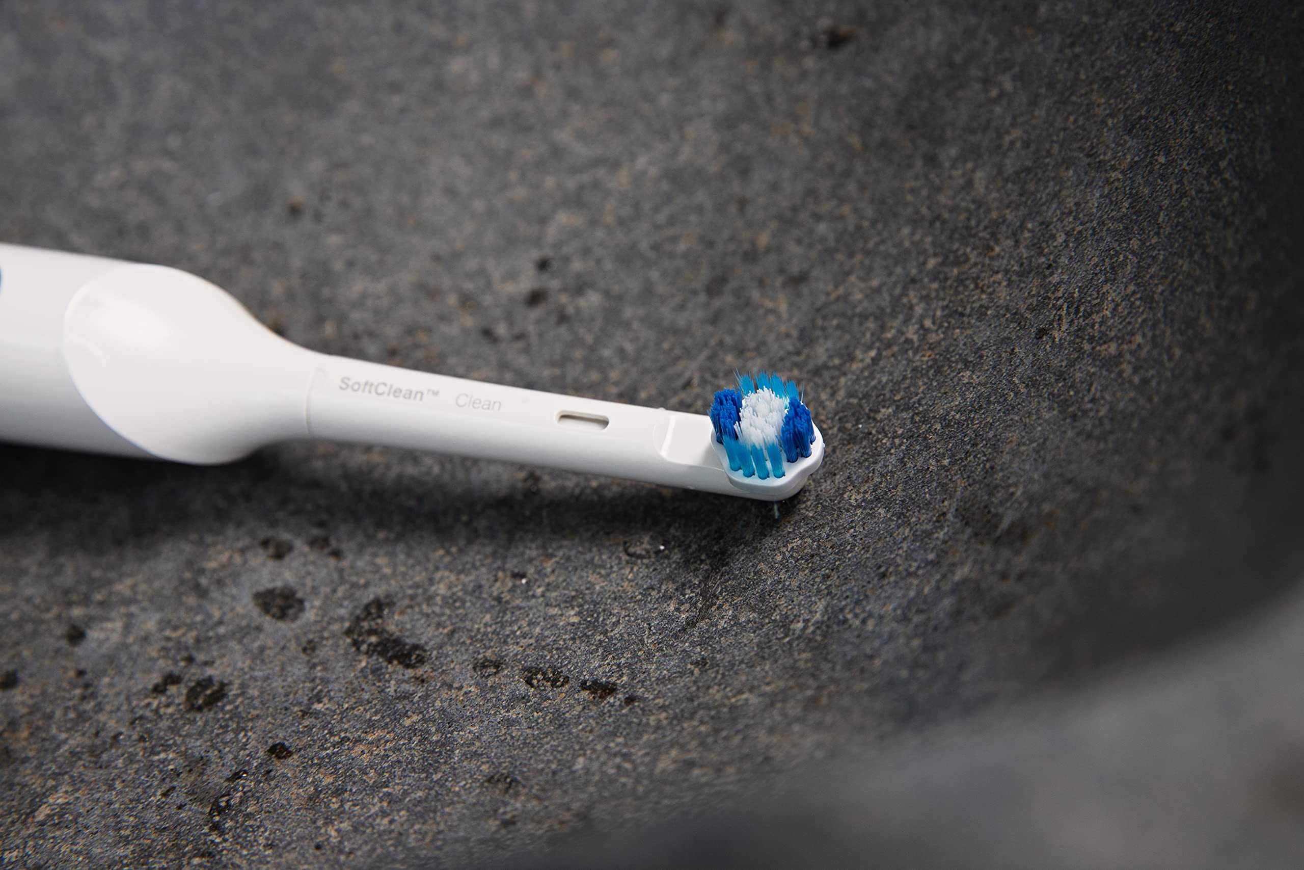 Jordan whitening electric toothbrush replacement head with blue and white bristles on white handle over dark stone sink