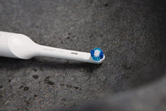 Jordan whitening electric toothbrush replacement head with blue and white bristles on white handle over dark stone sink